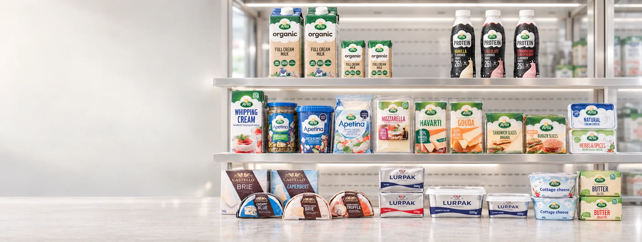 Arla, Castello and Lurpak products on a chilled display: organic milk, protein shakes, whipping cream, Apetina, mozzarella, havarti, gouda, cheese slices, brie, camembert, butter and cottage cheese